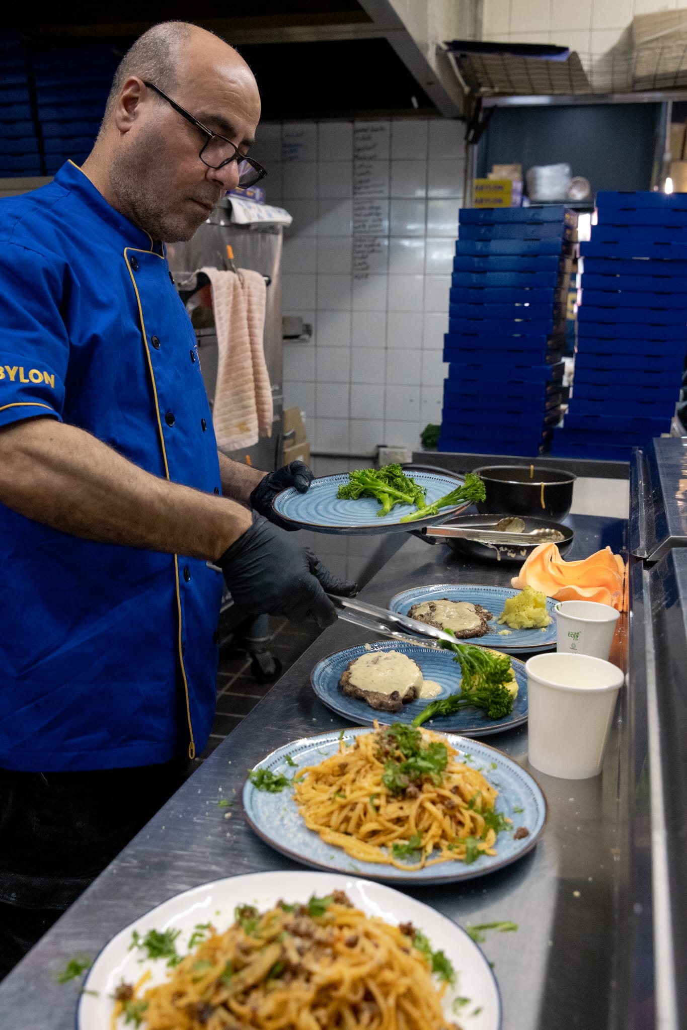 The owner of Babylon Bakery & Grill plating food in his branded chef's jacket